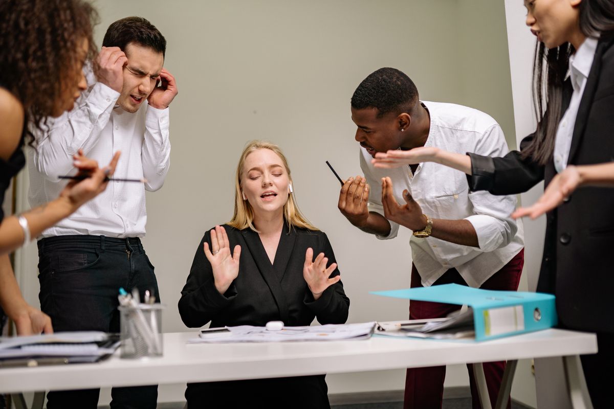 A small team gathered around a table in a workplace briefing, one person leading the conversation.