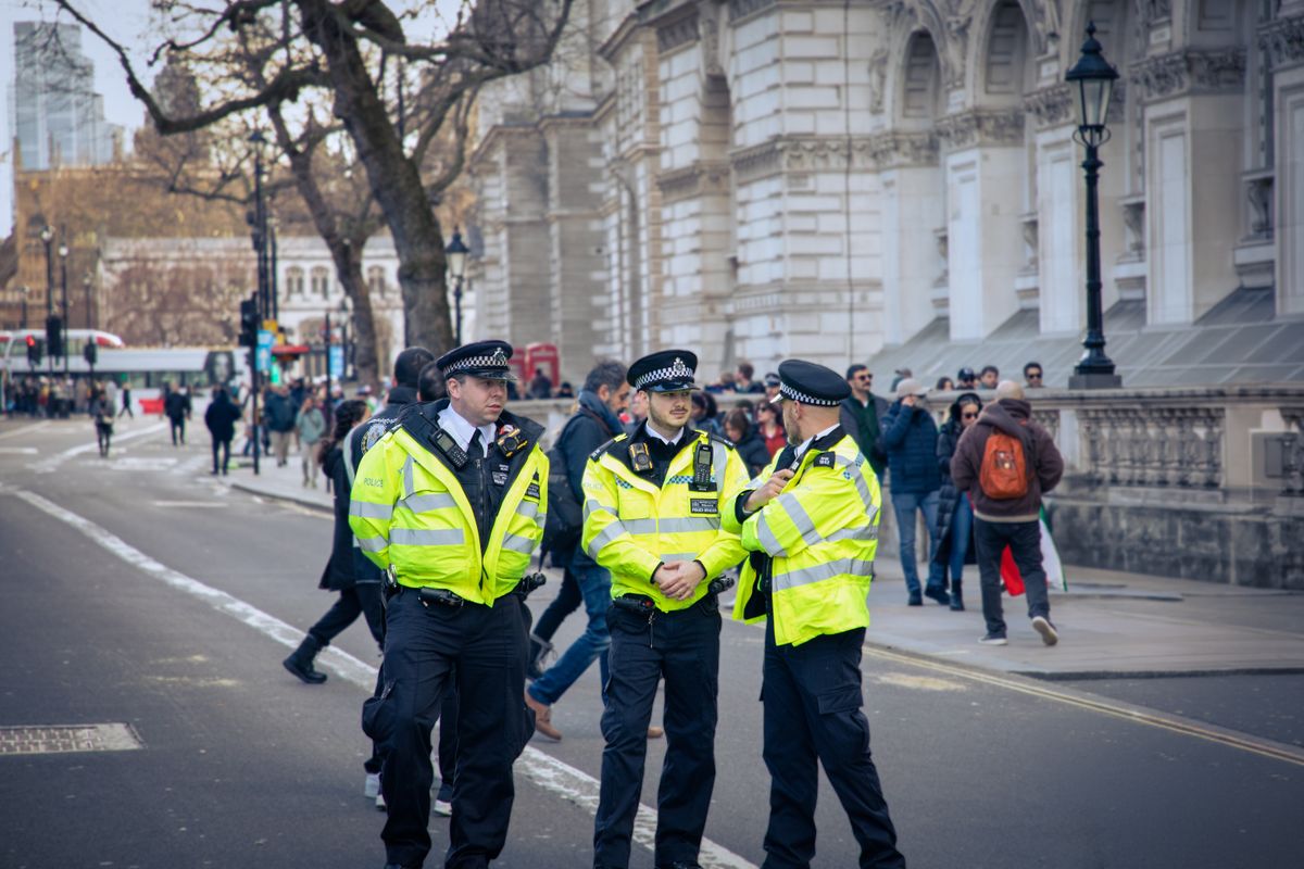 Three Metropolitan Police officers in high-visibility jackets conferring on a London street.