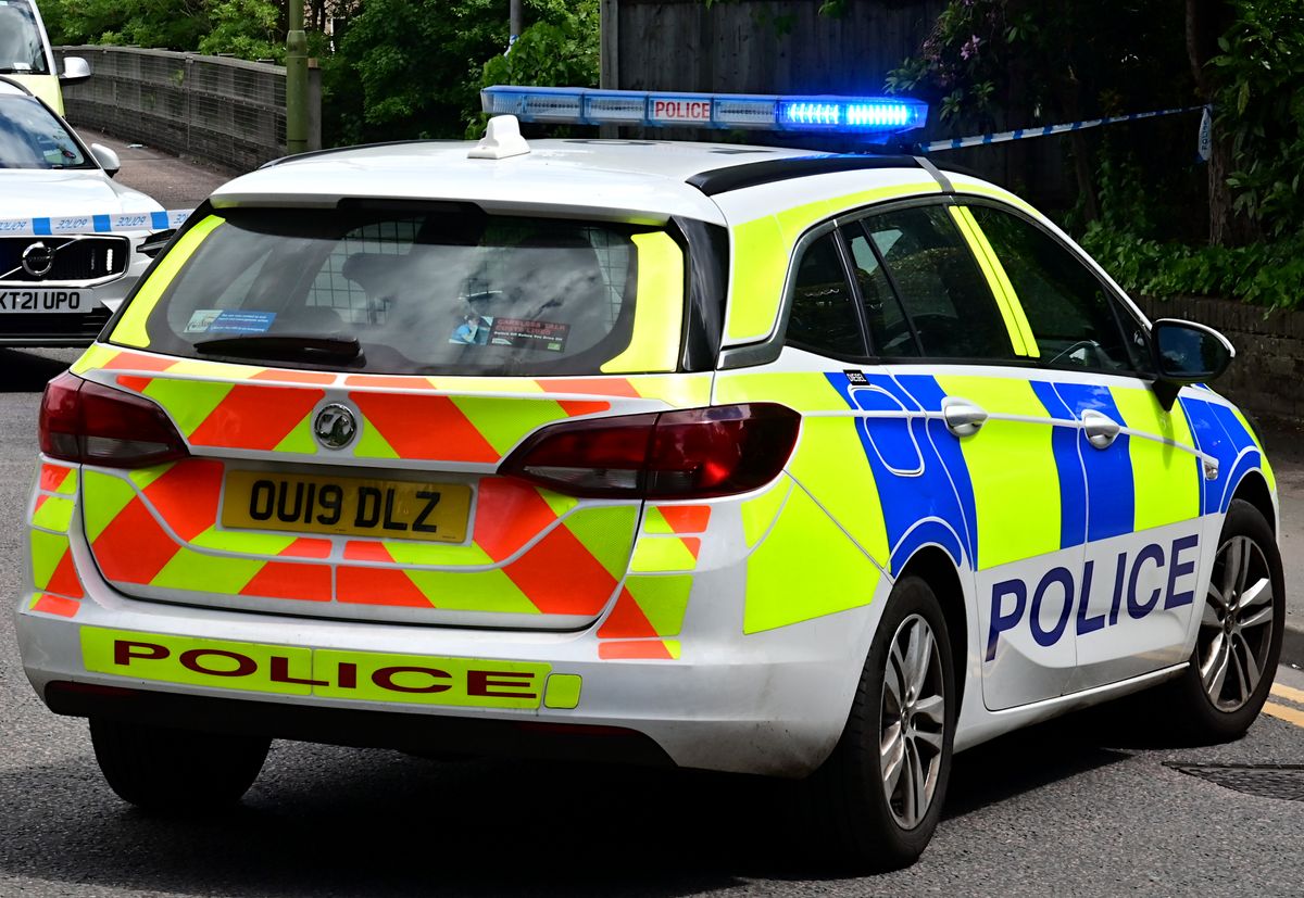A British police patrol car with blue lights on, marked POLICE in reflective Battenberg markings, on a residential street.