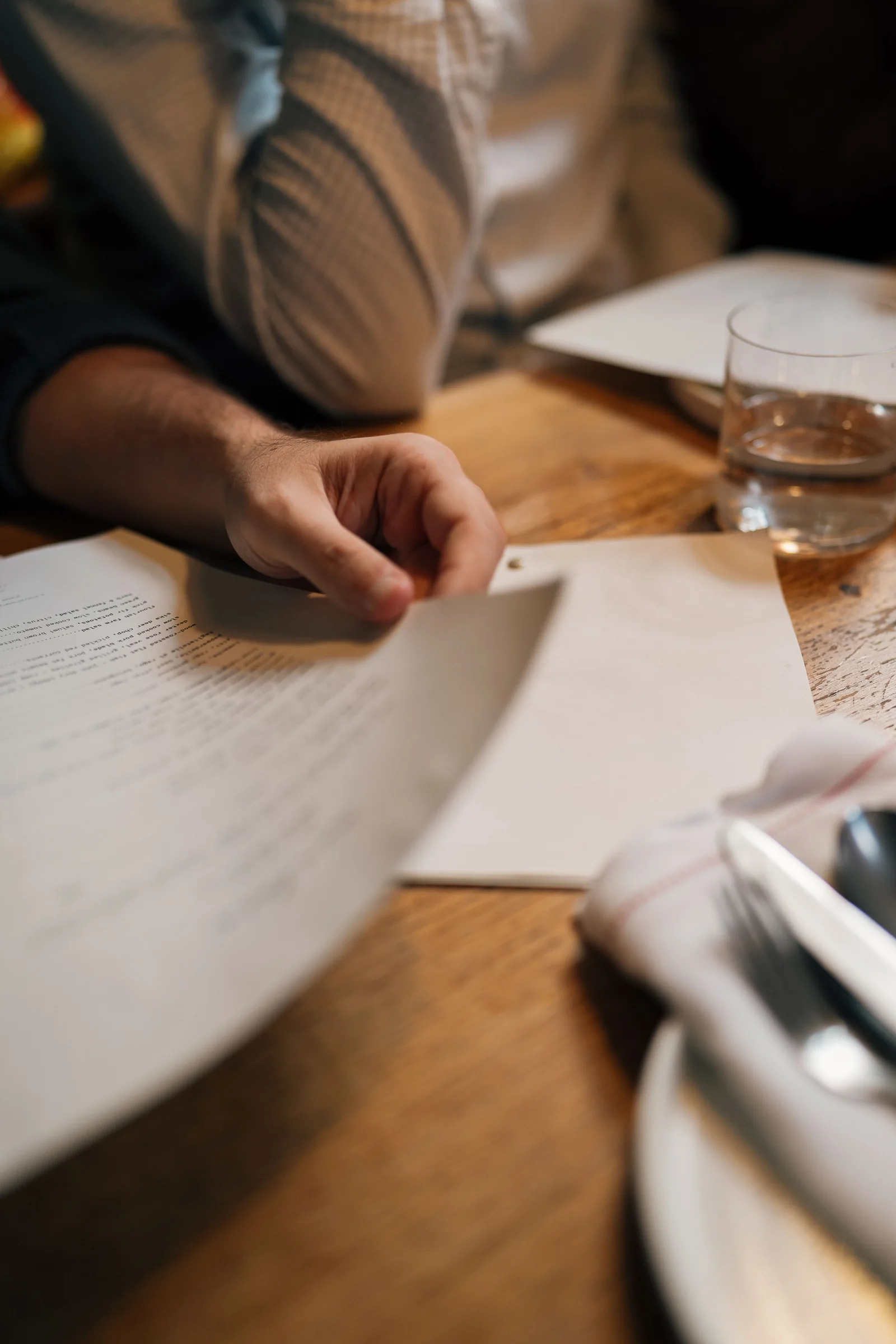 A person turning pages of a book at a wooden table.