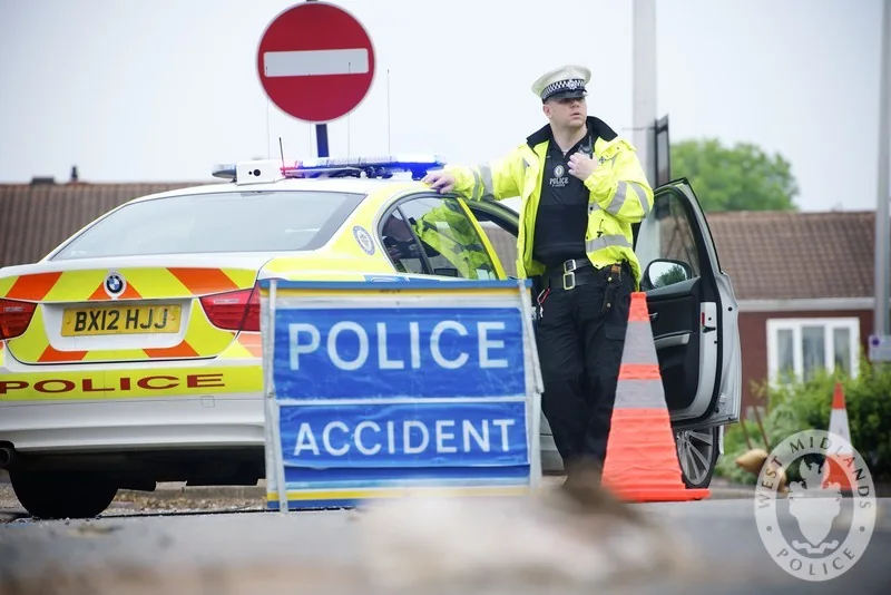 A West Midlands traffic officer beside a police car and an accident sign.